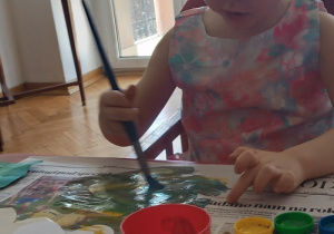 dziewczynka maluje farbami przy stoliku